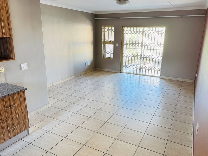 An open-plan living area featuring tiled floors, built-in kitchen cabinetry with granite countertops, and a sliding door leading to an outdoor space with security gates.