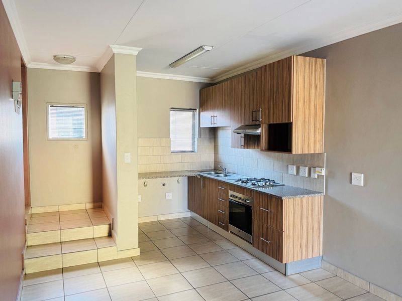 A clean, functional kitchen featuring wood-finish cabinetry, granite countertops, a built-in gas hob, oven, and tiled flooring in an open-plan layout.