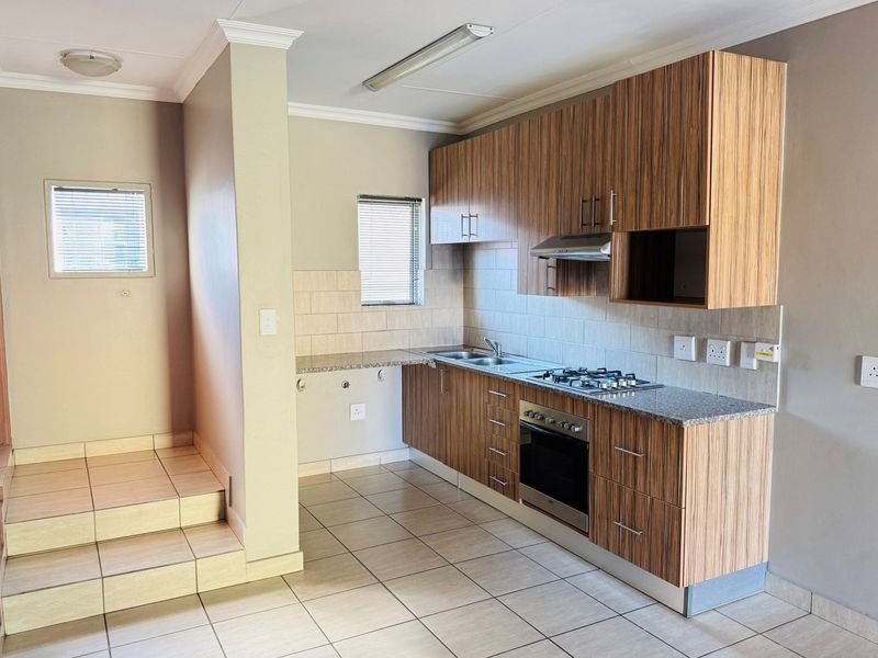 A clean, functional kitchen featuring wood-finish cabinetry, granite countertops, a gas hob, and built-in oven, with tiled flooring and backsplash.