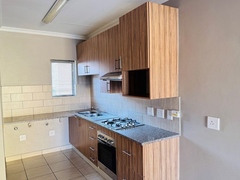 A clean, functional kitchen featuring wood-grain cabinetry, granite countertops, a gas hob, built-in oven, and tiled backsplash.