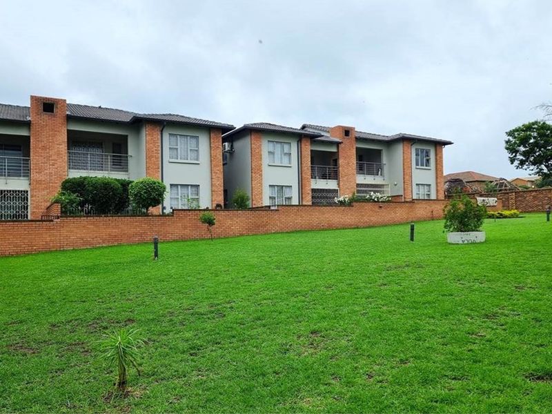 View of the rear apartment complex facade featuring brick construction, private balconies, and a well-maintained communal lawn area.