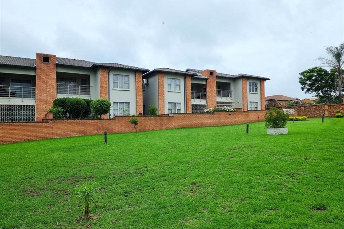 View of the rear apartment complex facade featuring brick construction, private balconies, and a well-maintained communal lawn area.