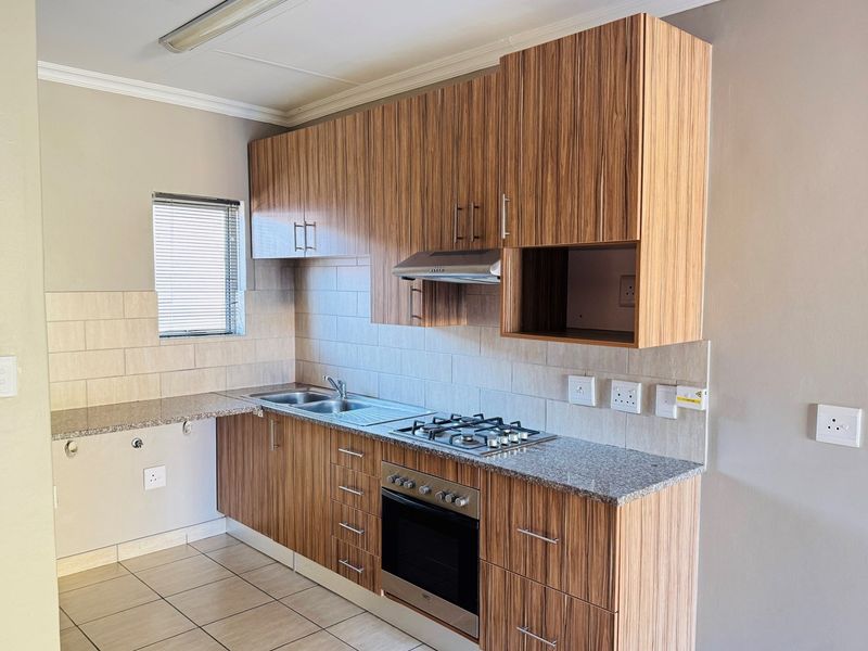 A clean, functional kitchen featuring wood-grain cabinetry, granite countertops, a gas hob, built-in oven, and tiled backsplash.