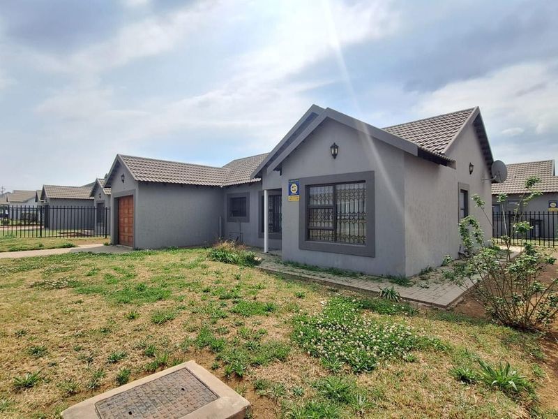 Front view of a single-story house featuring a tiled roof, grey exterior finish, garage, and perimeter fencing with a paved walkway.