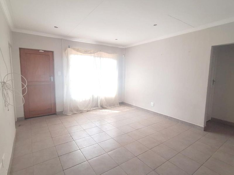 An empty living room featuring tiled flooring, recessed downlights, and coved ceiling cornices, offering a blank canvas for interior design.