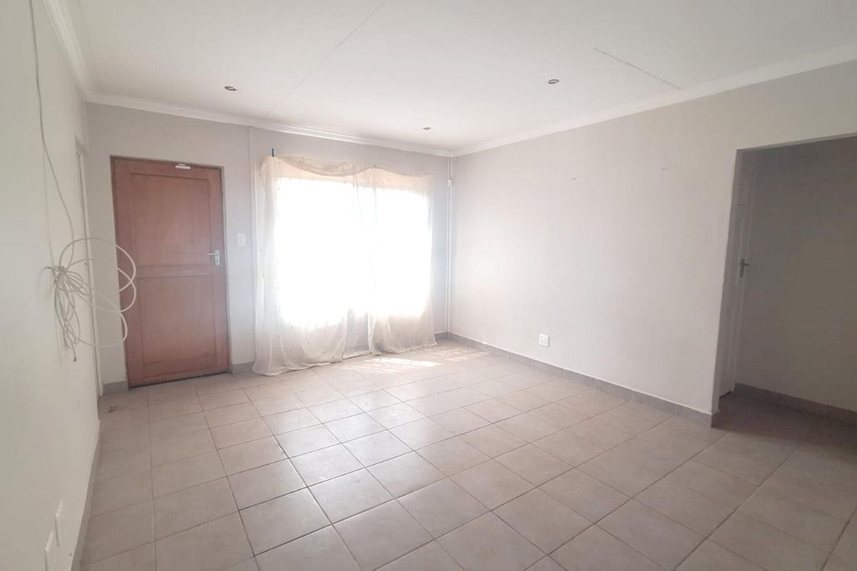 An empty living room featuring tiled flooring, recessed downlights, and coved ceiling cornices, offering a blank canvas for interior design.