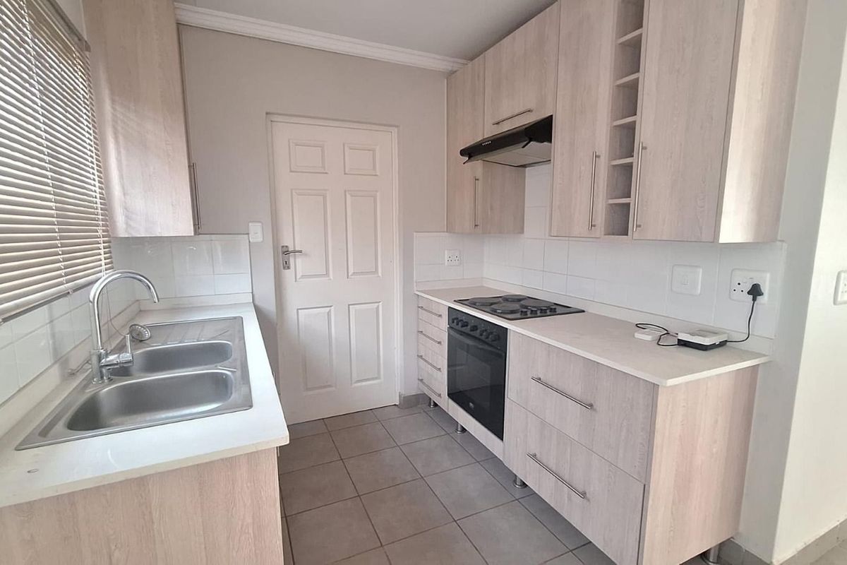 A clean and functional kitchen featuring light wood-finish cabinetry, a built-in oven with hob, extractor fan, and a double sink with tiled splashback.