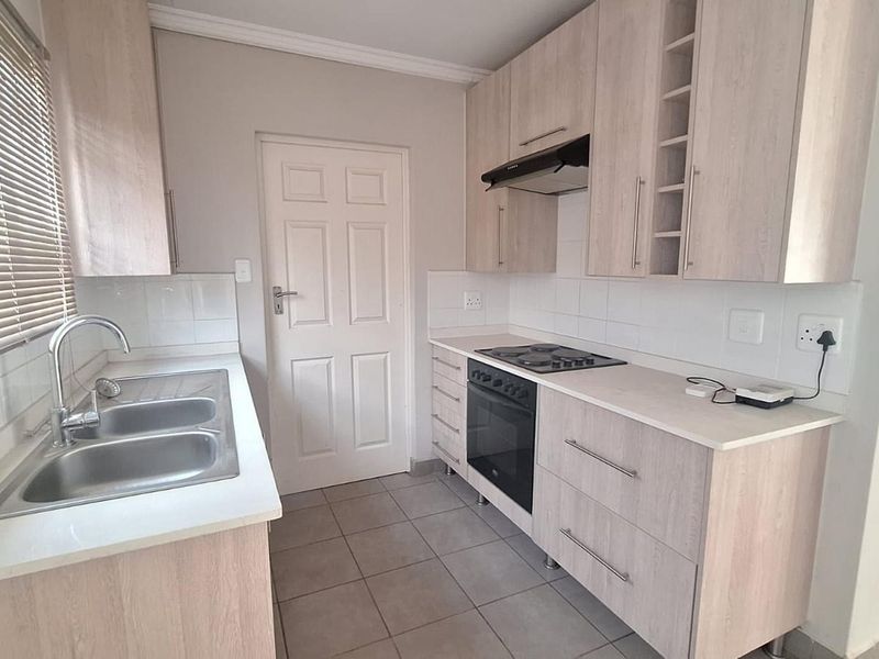 A clean and functional kitchen featuring light wood-finish cabinetry, a built-in oven with hob, extractor fan, and a double sink with tiled splashback.