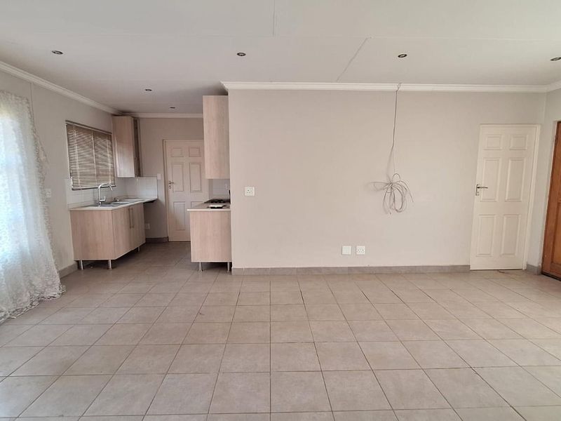 An open-plan living and kitchen area featuring tiled flooring, built-in cabinetry, and neutral finishes, providing a blank canvas for interior design.
