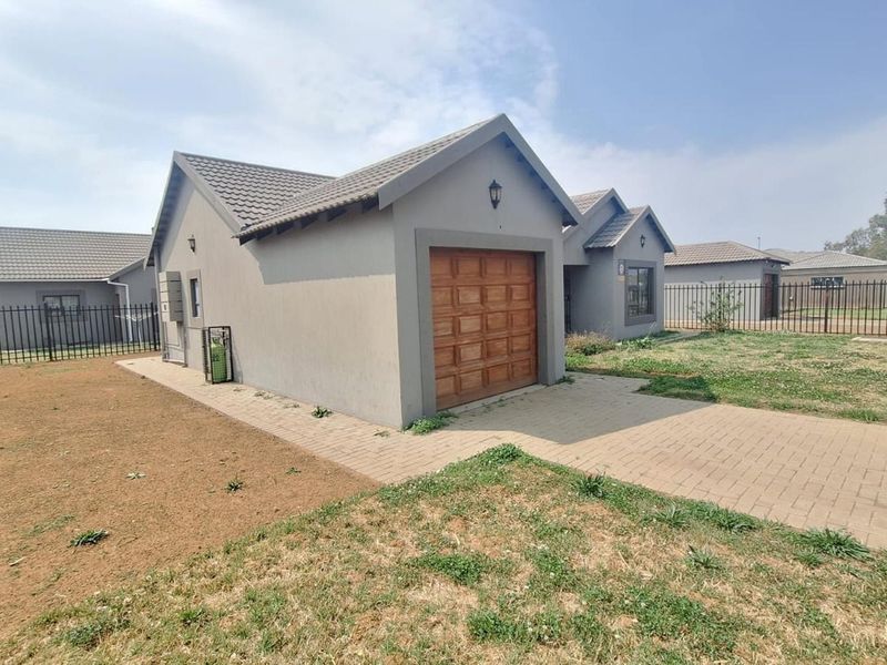 Front view of a single-story house featuring a tiled roof, a single garage, a paved driveway, and metal perimeter fencing.