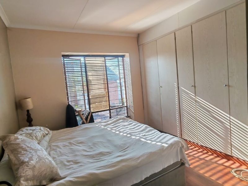 A bedroom featuring laminate flooring, built-in cupboards, and venetian blinds, offering a functional space with natural light.