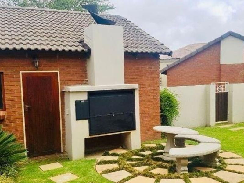 Rear exterior view featuring a brick facade, a built-in braai area with a chimney, and a landscaped garden with stone paving.