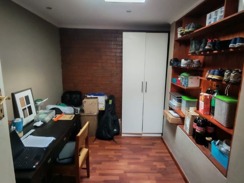 A functional home office featuring built-in shelving, a built-in wardrobe, an exposed brick feature wall, and durable laminate flooring.