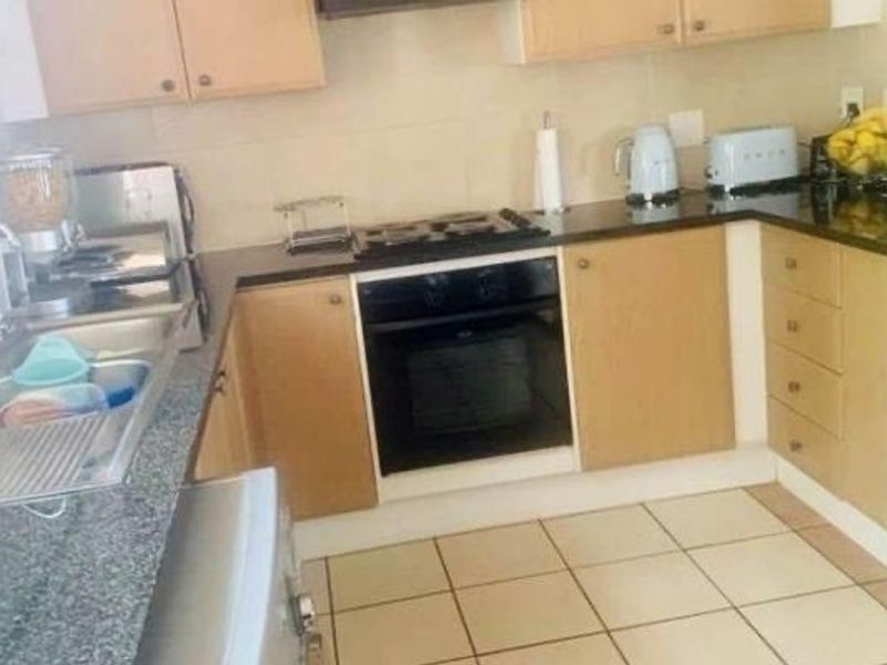 A functional kitchen featuring light wood cabinetry, granite countertops, a built-in oven with gas hob, and tiled flooring.