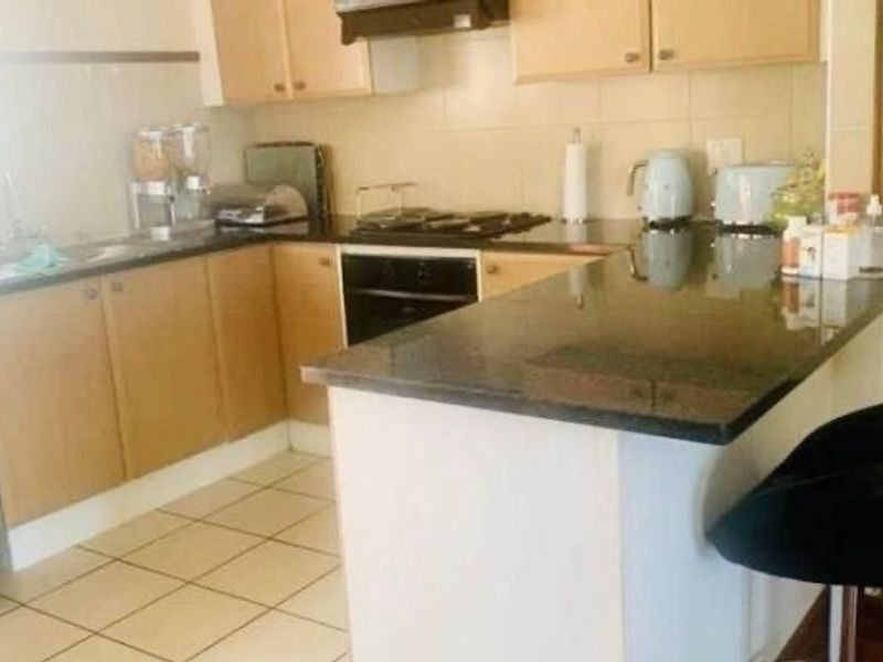 A functional kitchen featuring light wood cabinetry, dark granite countertops, a built-in oven with hob, and tiled flooring with a breakfast bar area.