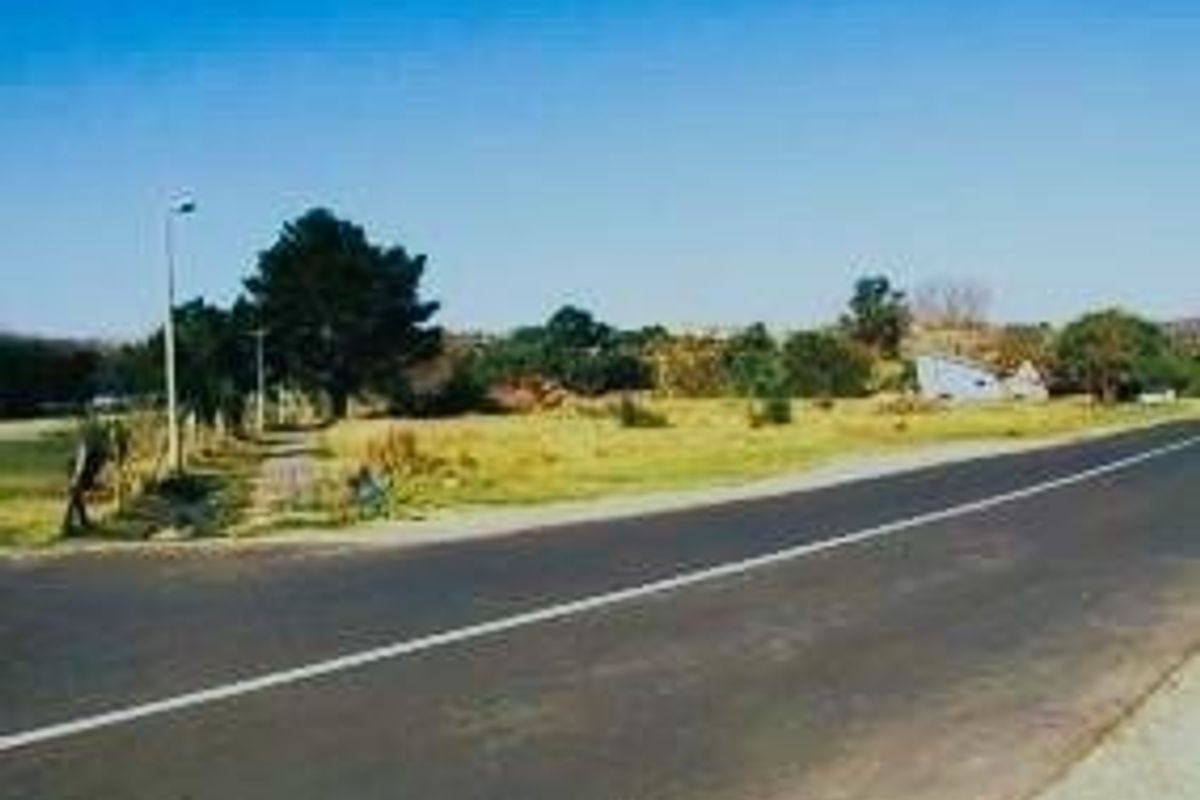 A street-level view of a vacant residential plot adjacent to an asphalt road with existing street lighting and perimeter fencing.