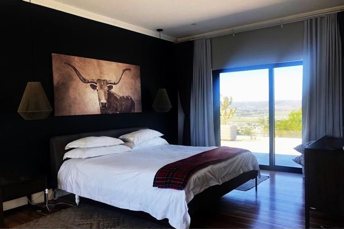 A modern bedroom featuring dark accent walls, hardwood flooring, and large sliding glass doors that provide natural light and scenic outdoor views.