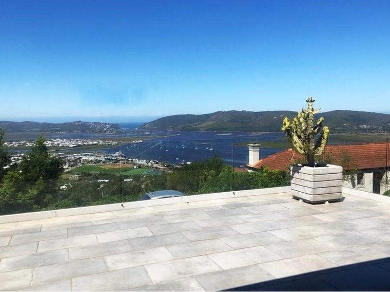 Spacious outdoor patio featuring stone tiling and a modern glass balustrade, offering expansive panoramic views of the estuary and surrounding landscape.