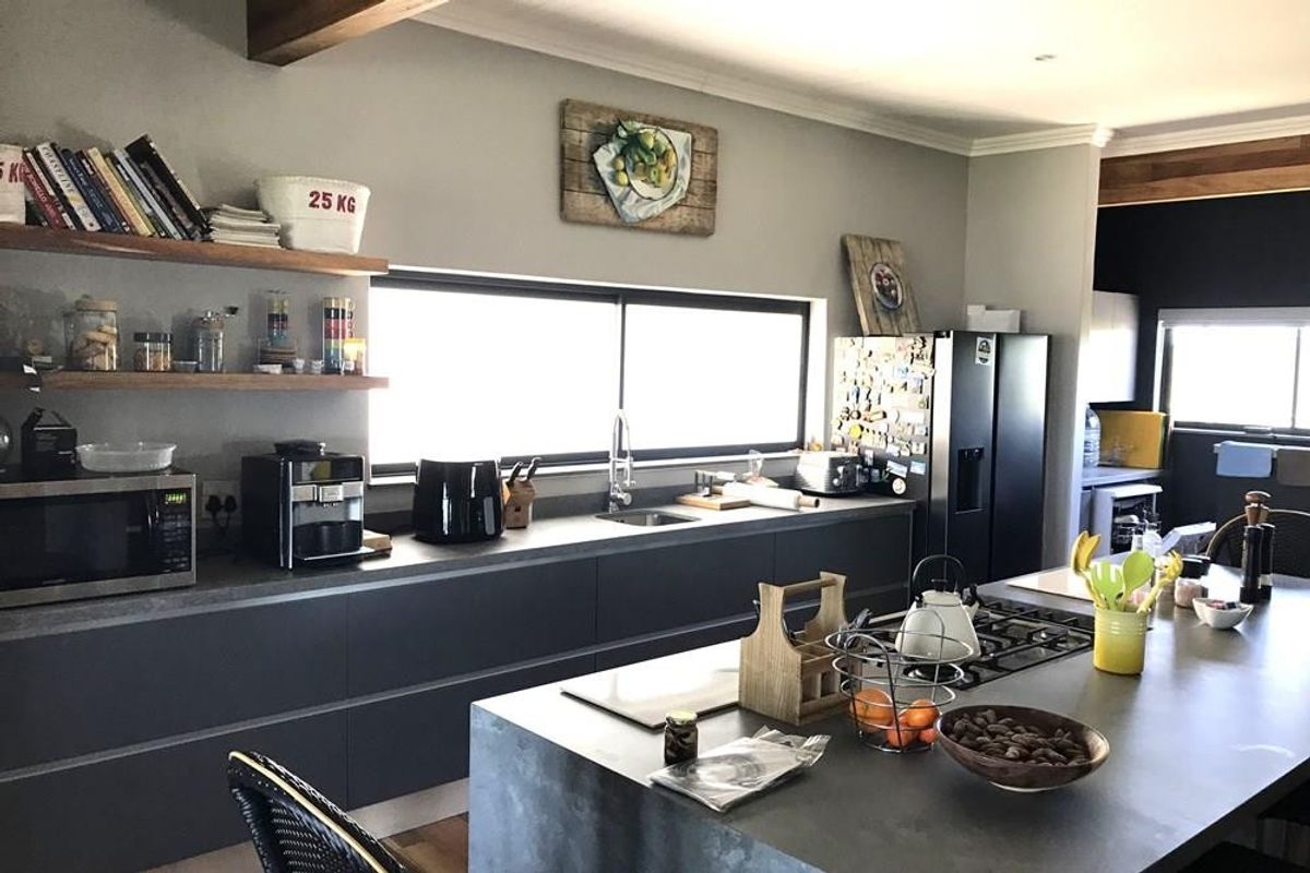 Modern kitchen featuring dark cabinetry, stone countertops, a central island with a gas cooktop, and floating timber shelving under an exposed ceiling beam.