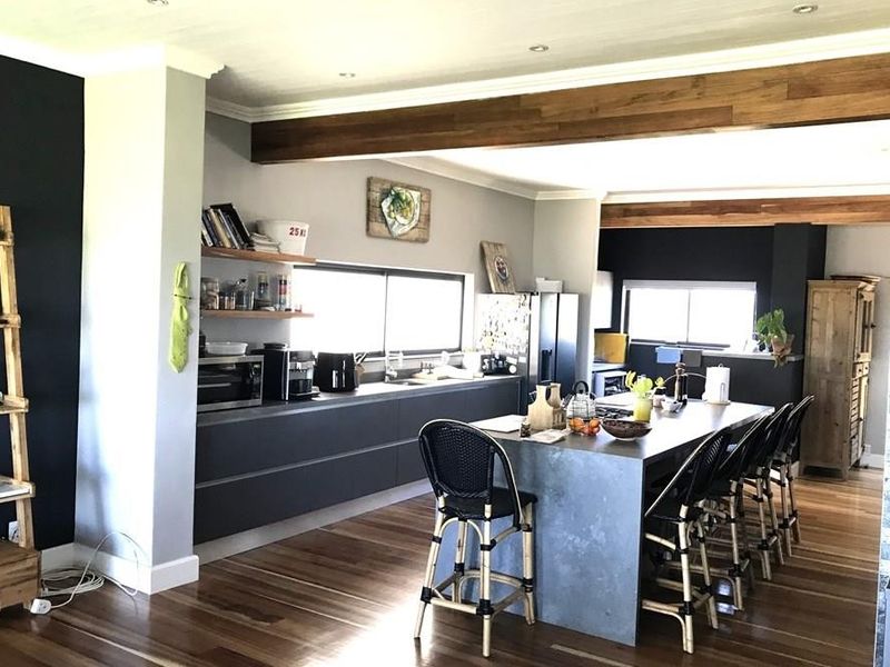 Spacious open-plan kitchen featuring modern dark cabinetry, a large central island, timber flooring, and exposed ceiling beams, creating a warm and contemporary living space.