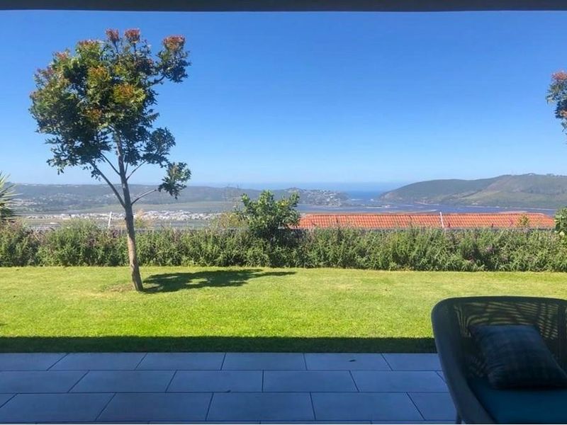 A scenic view from a tiled patio overlooking a well-maintained garden with expansive coastal and estuary vistas.