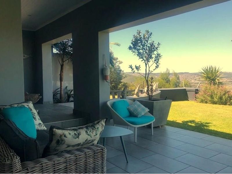 A spacious covered patio featuring tiled flooring and concrete pillars, offering an open-air transition to the garden with scenic landscape views.