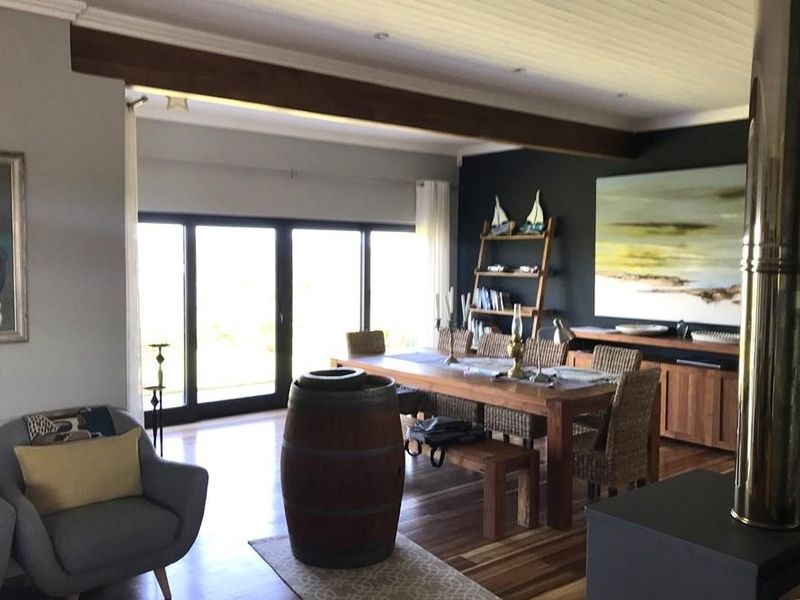 Spacious open-plan living and dining area featuring warm timber flooring, exposed ceiling beams, and a modern freestanding fireplace with large sliding glass doors.