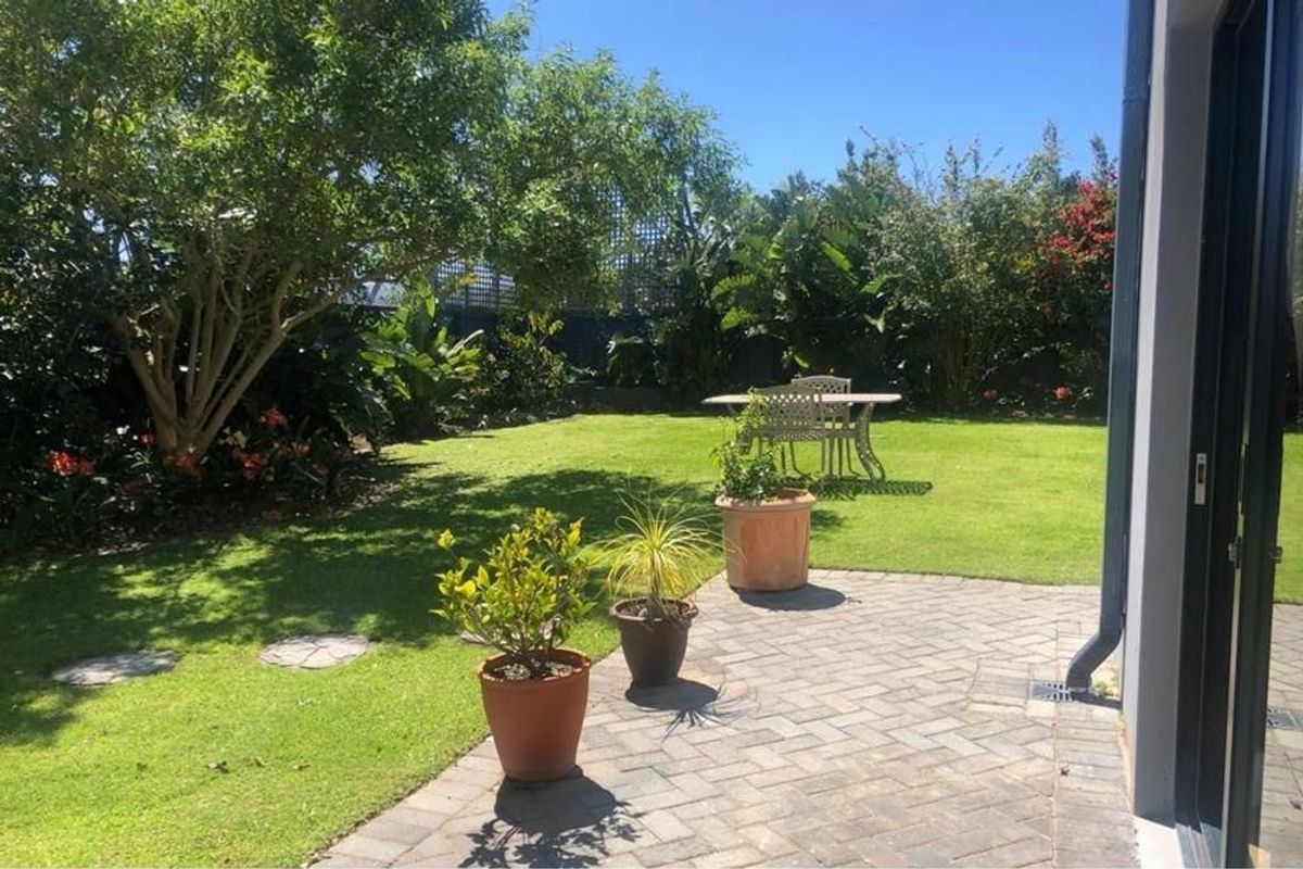 A well-maintained rear garden featuring a paved patio area, lush lawn, and established perimeter landscaping.