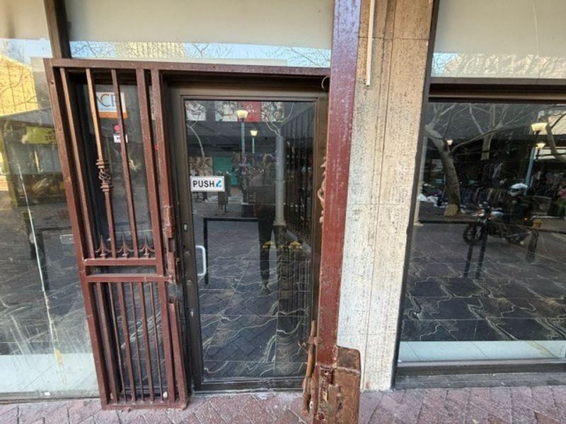 Retail storefront entrance featuring a glass door with a metal security gate and large display windows set into a stone facade.