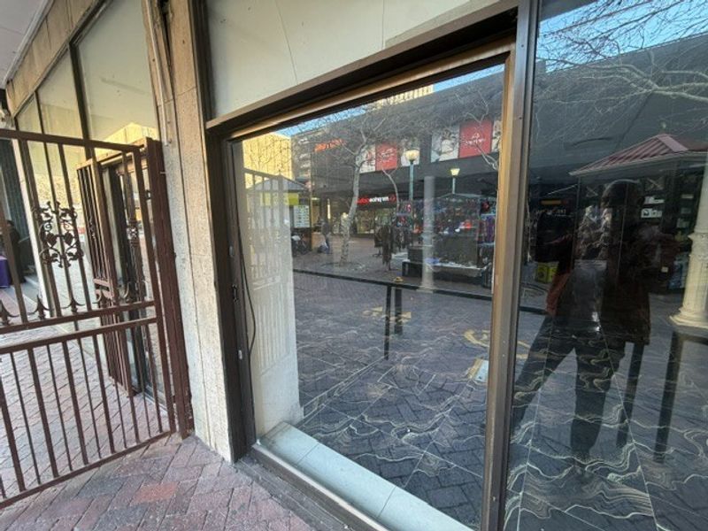 Retail storefront featuring a large display window and metal security gate, situated along a paved pedestrian walkway.