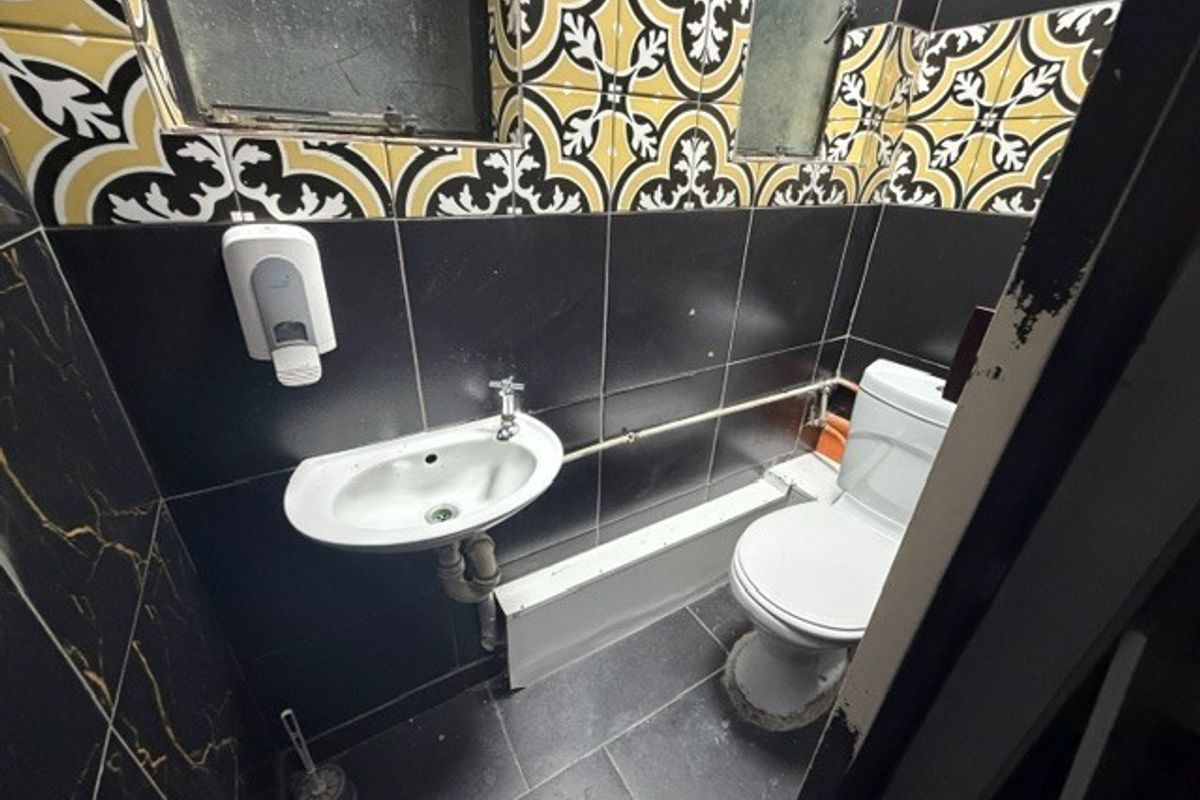 A small, functional bathroom featuring black and patterned wall tiles, a wall-mounted basin, and a standard toilet.