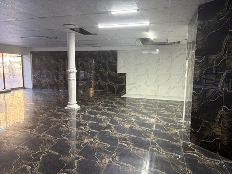 Spacious open-plan retail area featuring high-gloss marble-effect floor and wall tiles, a decorative central column, and a suspended ceiling with integrated lighting.