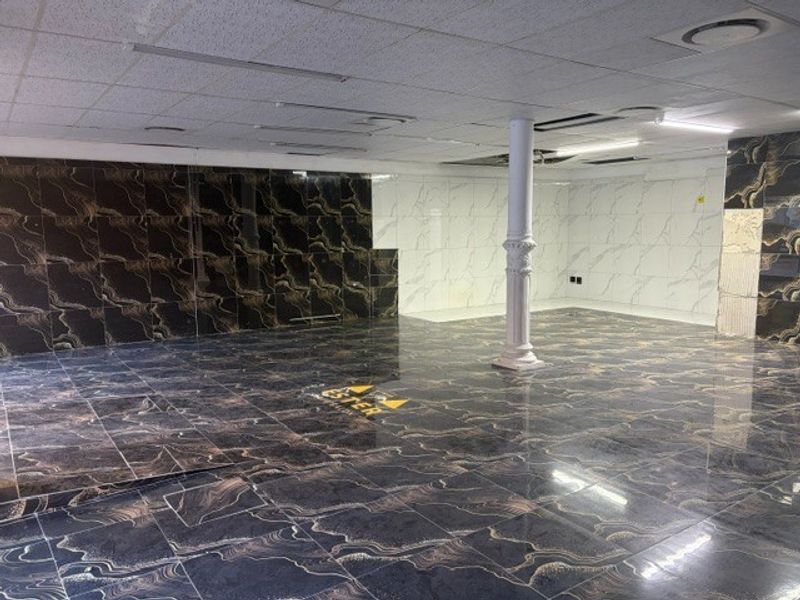 An open-plan retail space featuring high-gloss marble-effect floor and wall tiles, a suspended ceiling, and a central structural column.