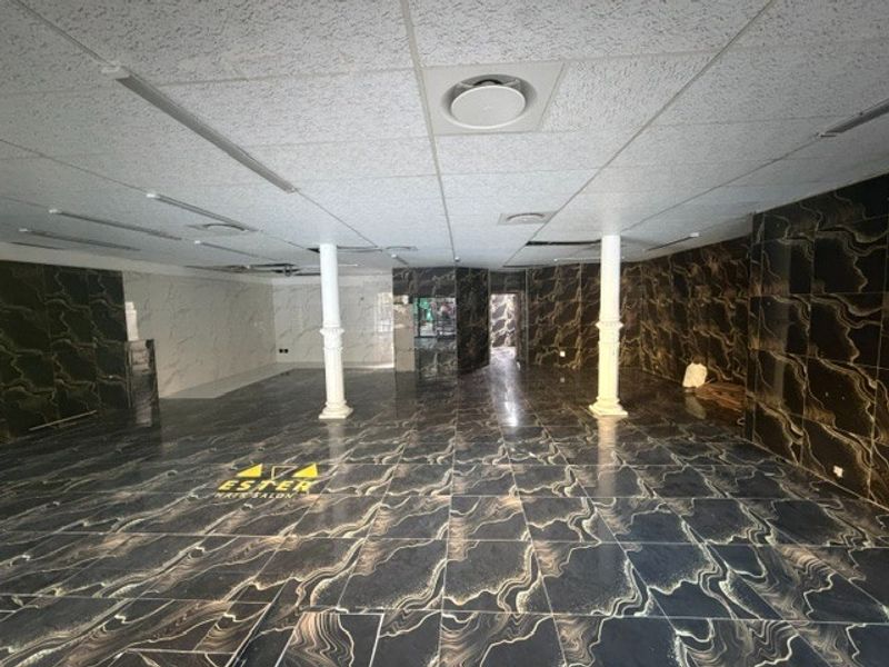 Spacious open-plan retail area featuring marble-effect floor and wall tiling, structural columns, and a suspended ceiling with integrated lighting and air conditioning.