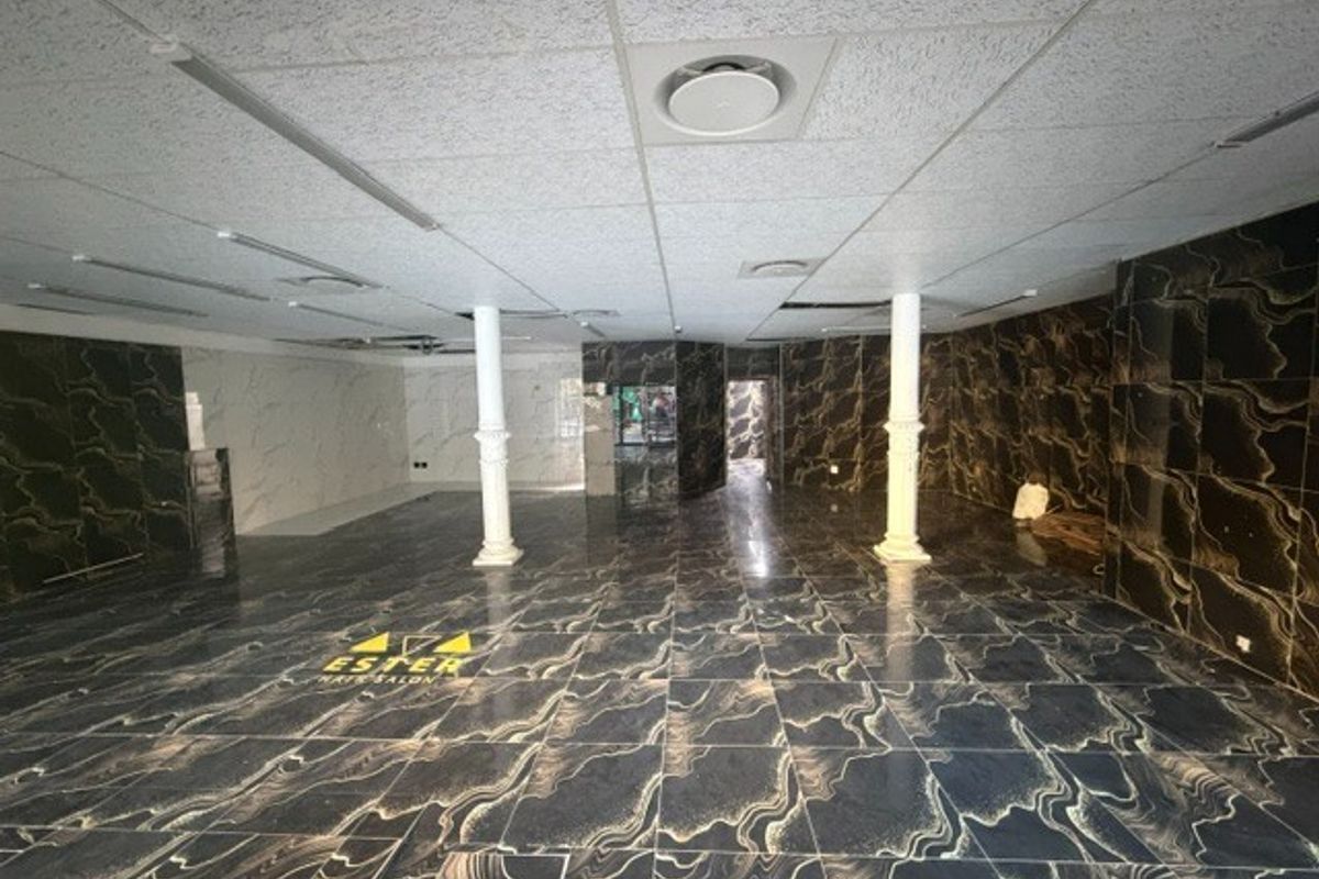 Spacious open-plan retail area featuring marble-effect floor and wall tiling, structural columns, and a suspended ceiling with integrated lighting and air conditioning.