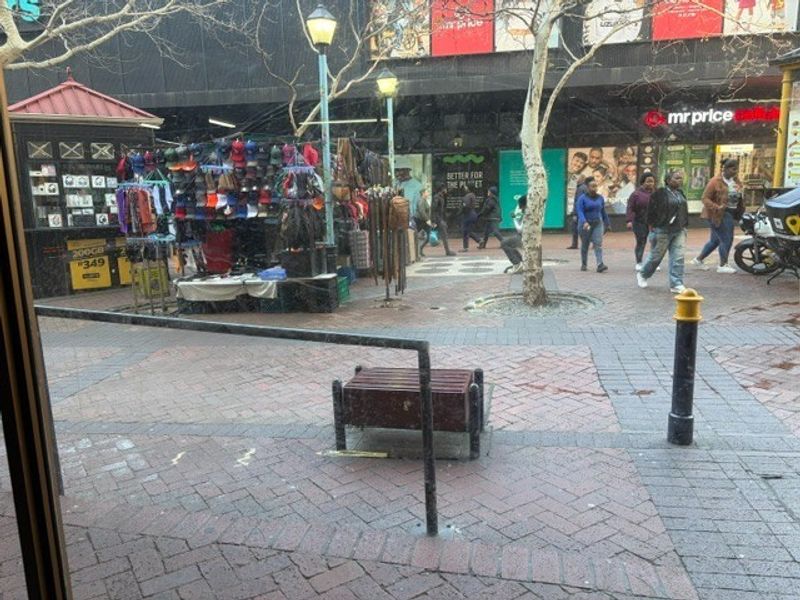 An outdoor pedestrian walkway area featuring brick paving, street lighting, and metal safety railings in a retail environment.