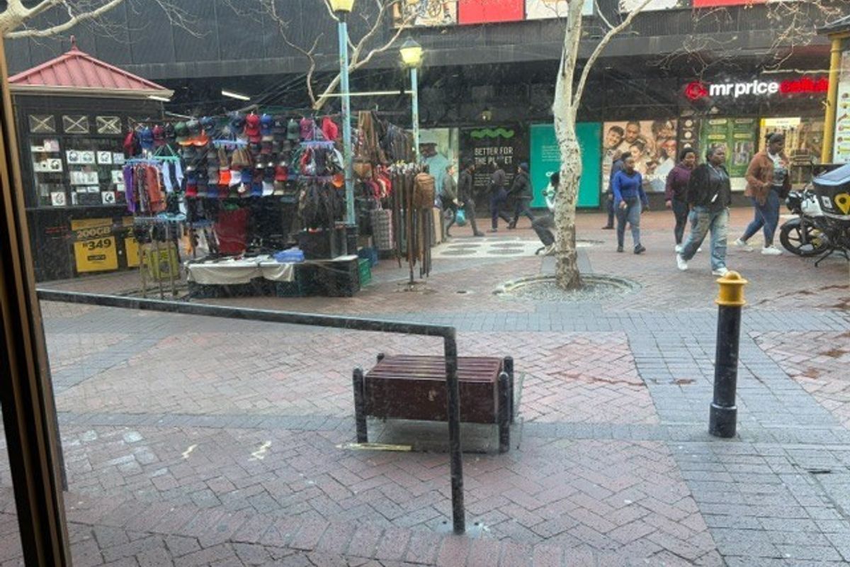 An outdoor pedestrian walkway area featuring brick paving, street lighting, and metal safety railings in a retail environment.