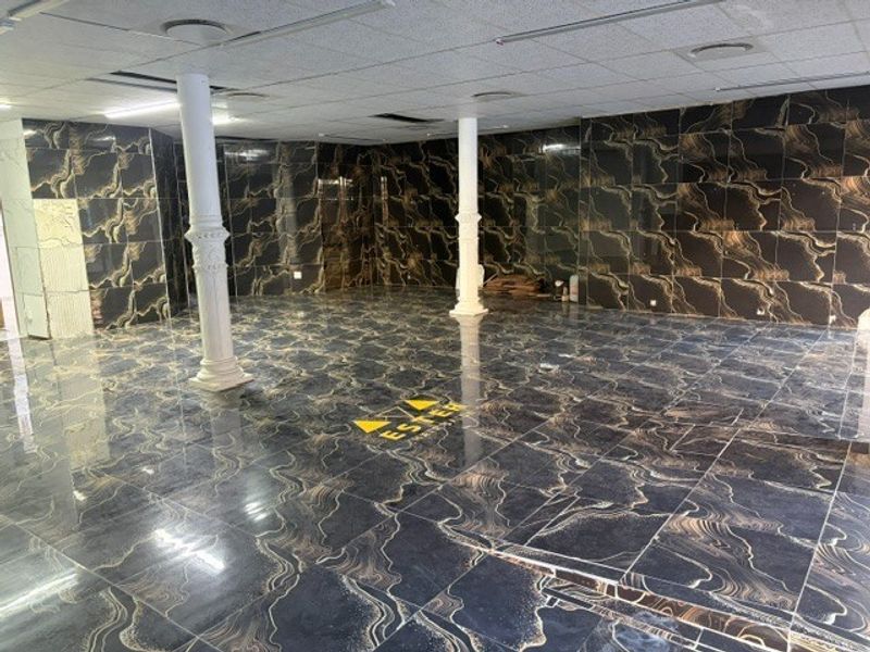 Spacious open-plan retail area featuring high-gloss marble-effect wall and floor tiling, decorative columns, and a suspended ceiling with recessed lighting.