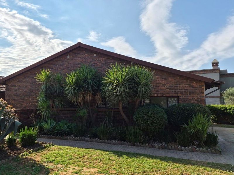 A well-maintained face brick apartment exterior featuring a pitched roof, diamond pane windows, and a neat paved walkway surrounded by established garden landscaping.