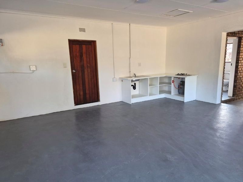 Open-plan living area featuring a basic kitchenette with a sink and gas hob, concrete flooring, and access to an adjoining bathroom.
