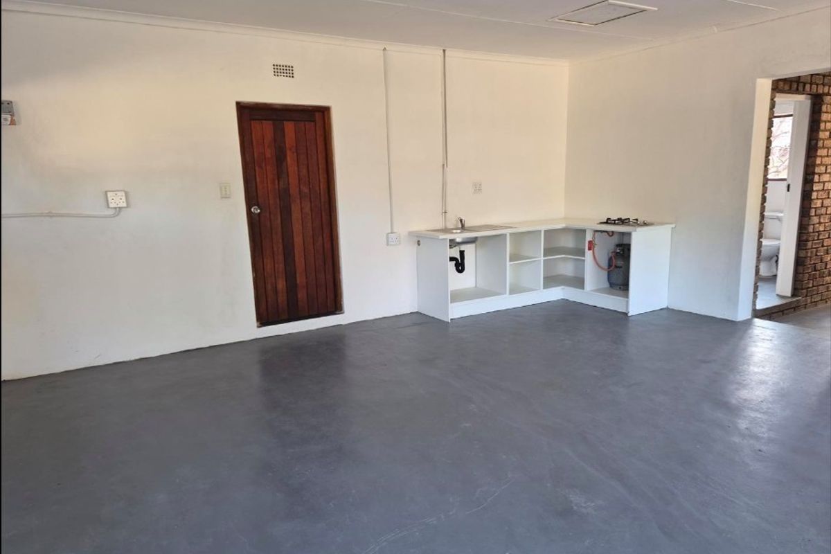 Open-plan living area featuring a basic kitchenette with a sink and gas hob, concrete flooring, and access to an adjoining bathroom.
