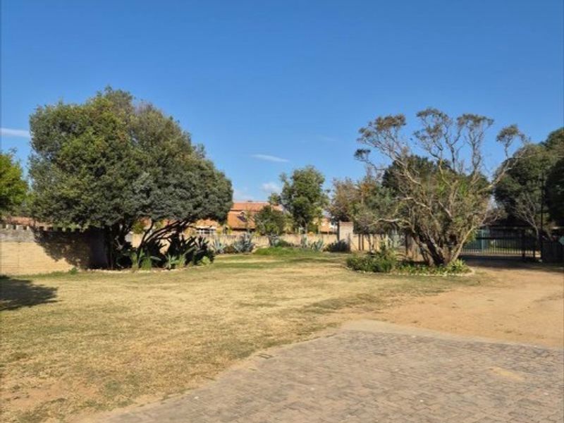 A spacious front exterior area featuring a paved driveway, established trees, and a boundary wall with gated access.