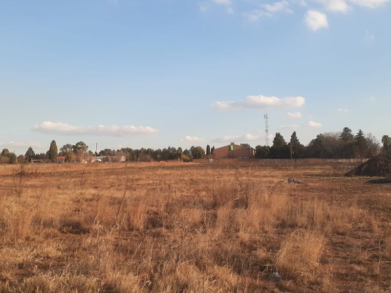 Expansive open land area suitable for development, featuring dry grass and distant perimeter fencing.