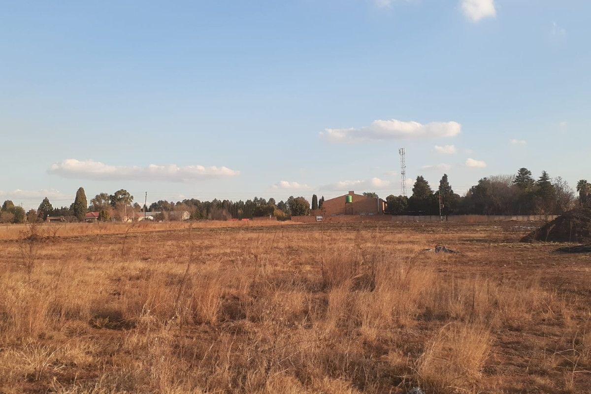 Expansive open land area suitable for development, featuring dry grass and distant perimeter fencing.
