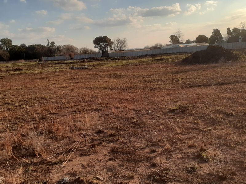 A wide, undeveloped plot of land featuring dry grass and perimeter fencing, offering significant potential for landscaping or future development.
