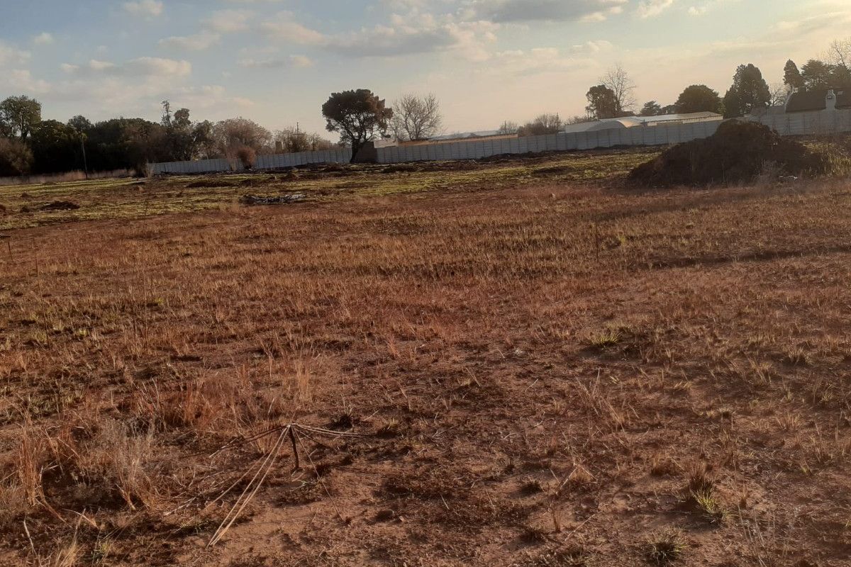 A wide, undeveloped plot of land featuring dry grass and perimeter fencing, offering significant potential for landscaping or future development.