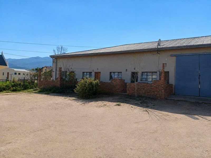 Exterior view of a commercial building featuring industrial sliding doors, brick boundary walls, and multiple individual unit entrances.