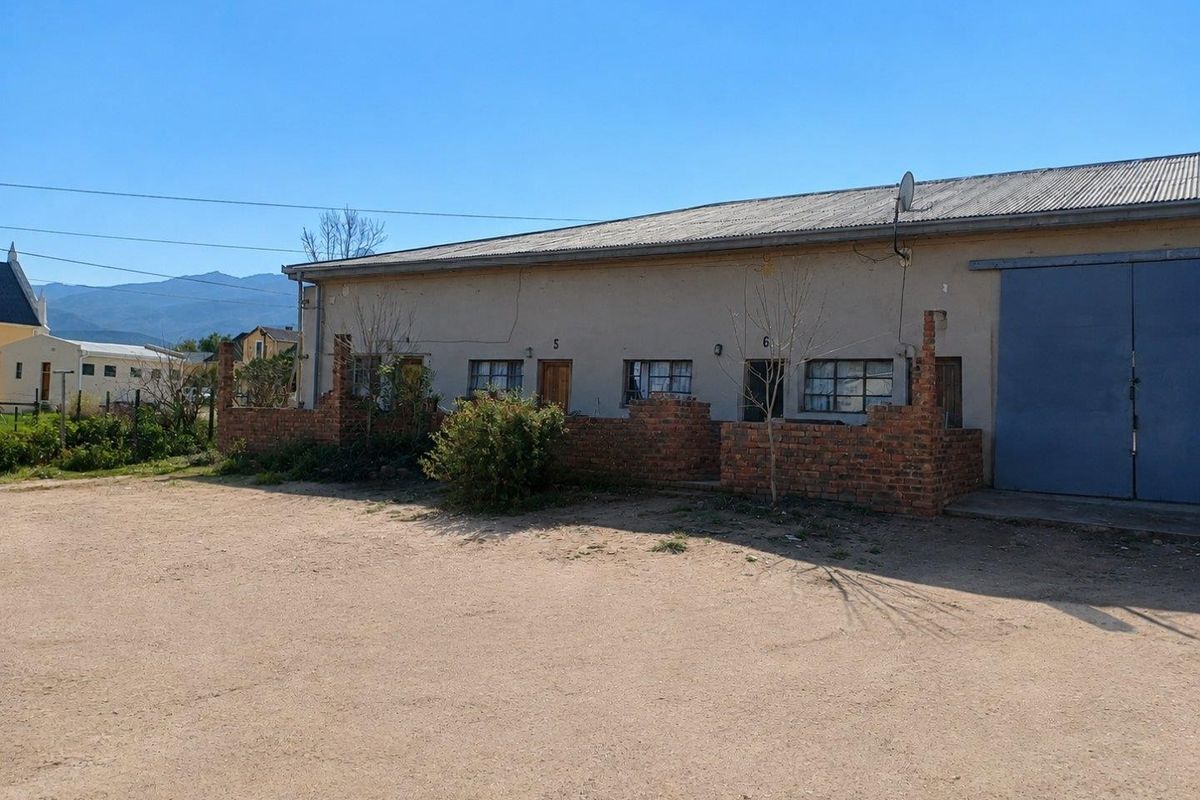 Exterior view of a commercial building featuring industrial sliding doors, brick boundary walls, and multiple individual unit entrances.