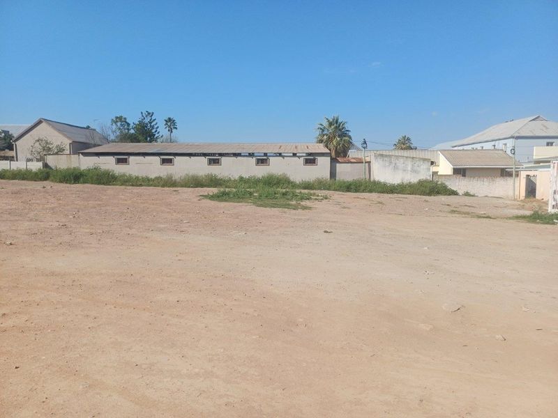 A wide view of a commercial property lot featuring a long, single-story structure with a corrugated roof and surrounding boundary walls.