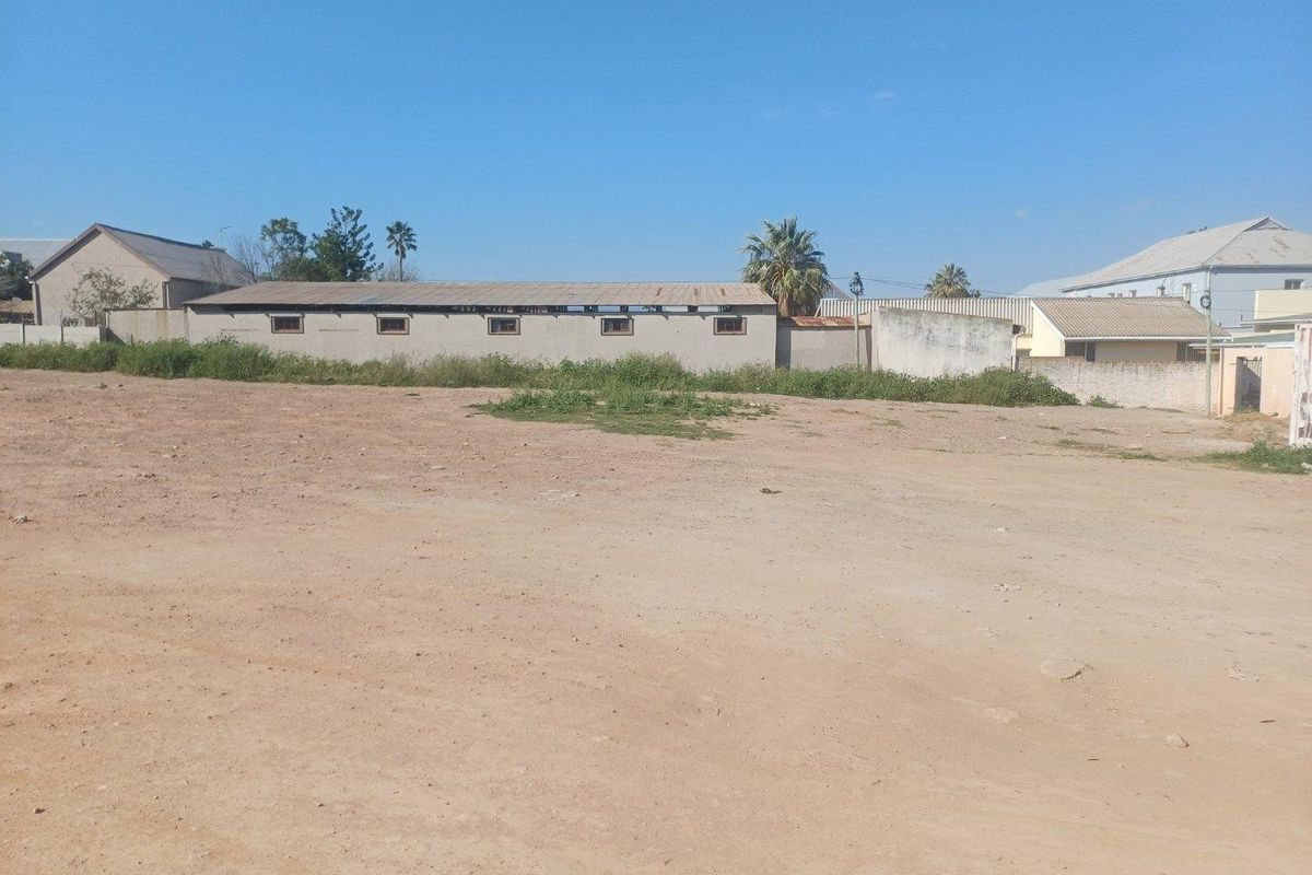 A wide view of a commercial property lot featuring a long, single-story structure with a corrugated roof and surrounding boundary walls.